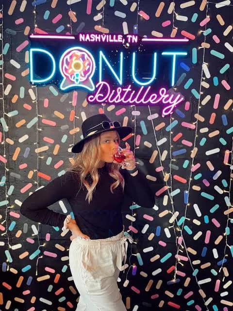 Guest posing at the neon Donut Distillery sign in Nashville
