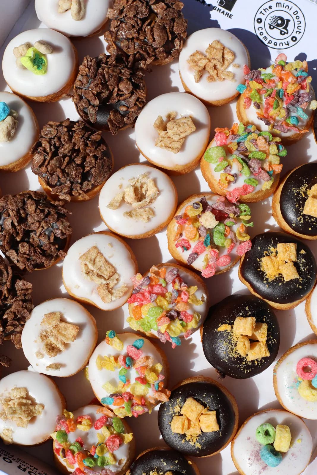 Box of mini donuts topped with colorful breakfast cereal